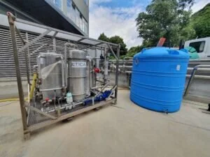 Impianto pilota industriale con serbatoi in acciaio e un grande serbatoio blu per il trattamento delle acque.