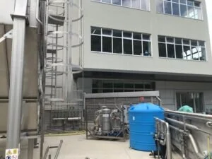 Vista esterna di un impianto industriale con serbatoio blu e macchinari tecnici presso il laboratorio di analisi.