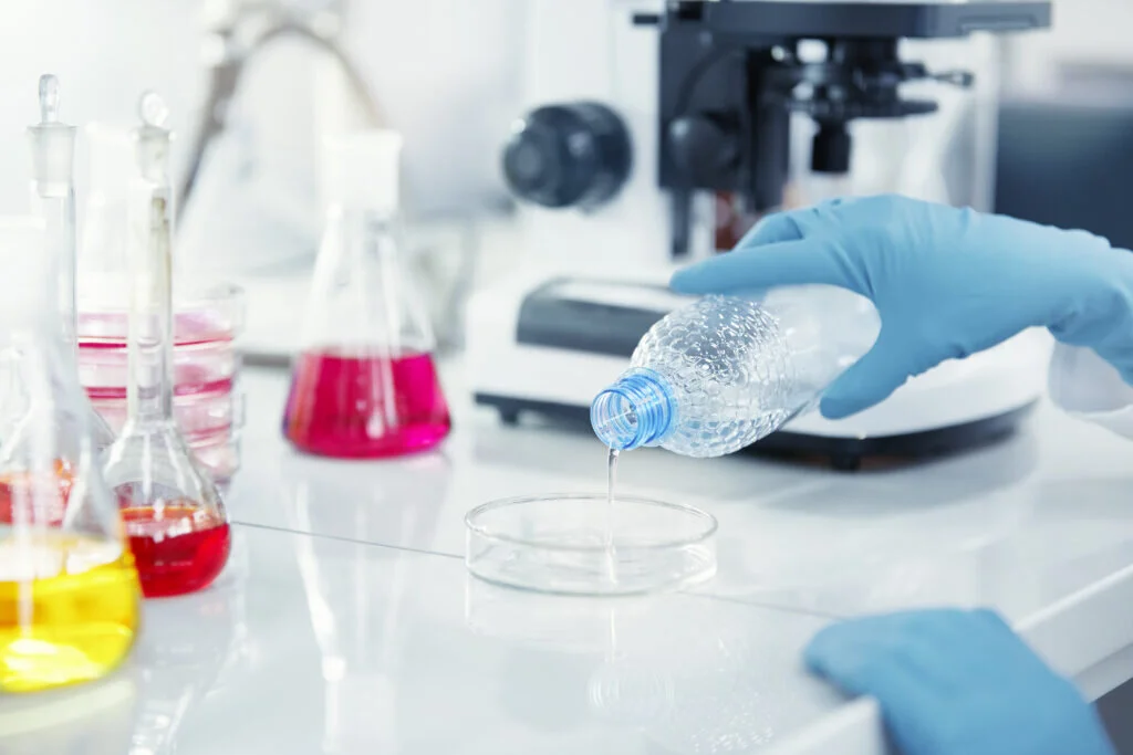Un chimico con guanti in lattice versa un liquido trasparente in una capsula di Petri durante i servizi analitici specialistici.